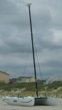 A tall, thin pole with a wire against a cloudy sky near houses.