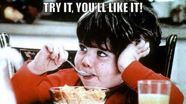 Child hesitantly trying food with a skeptical expression.